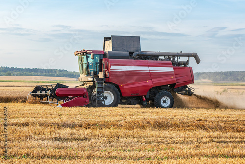 Red combine harvester harvesting wheat on agricultural field