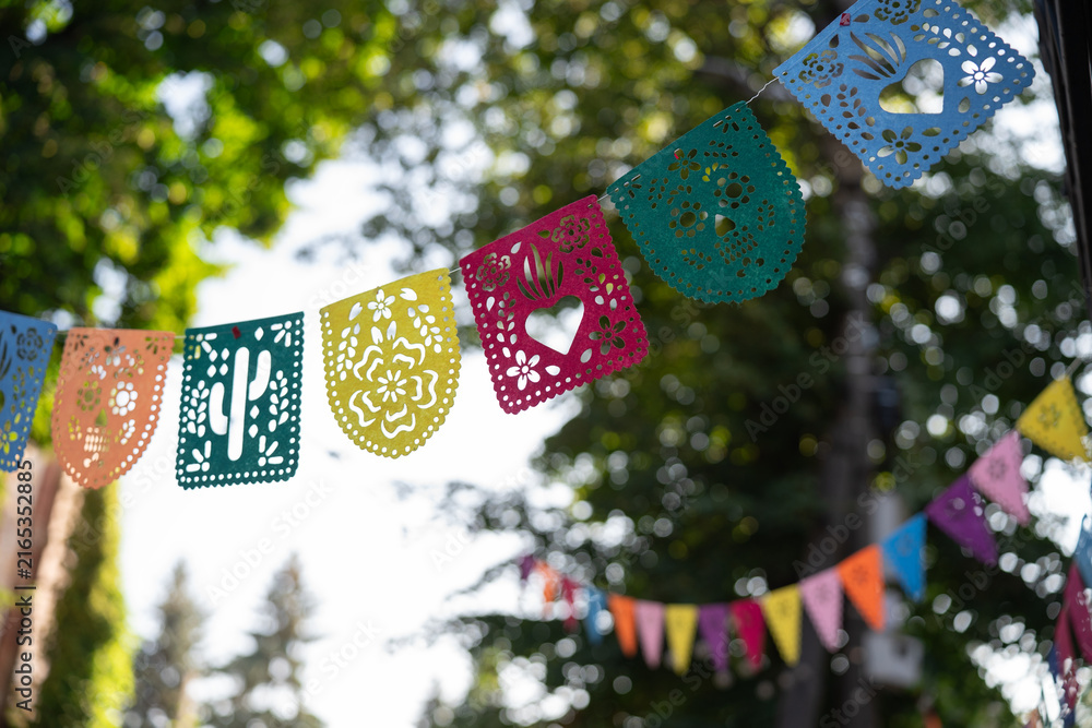 Fototapeta premium Vibrant festive Papel Picado garland with traditional cut-out patterns against a beautiful blurred bokeh background, design template for Day of the Dead celebration
