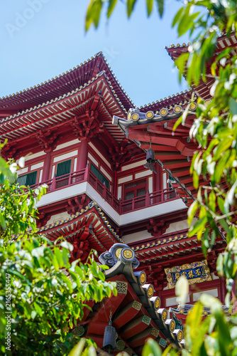Fotografie View between trees of a corner of the red and white Buddha Tooth Relic Temple in