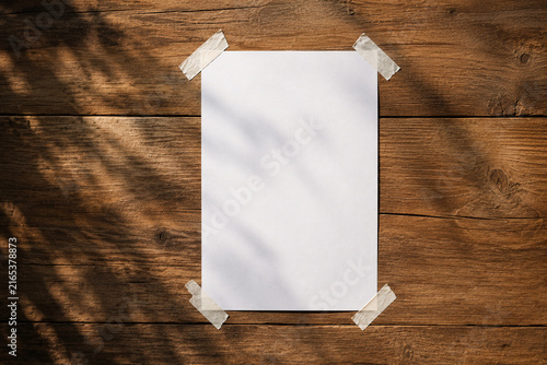 Blank white paper sheet taped with adhesive tape on a rustic wooden background mockup scotch tape sticky note wooden surface nature shadow wooden table template