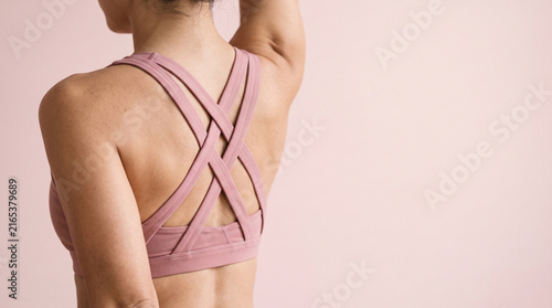 Back view of person in pink athletic gear with cross-back straps, close up studio shot. Fitness, healthy lifestyle, wellness, body care and gym training commercial photograph.