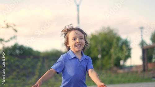 A boy in a blue shirt runs joyfully through the green landscape, smiling as he plays. The boy's excitement is visible in his expressions and movements.