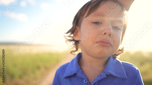 The boy stands on a path, showing sadness and tears. The boy's blue shirt contrasts with the bright background as he gazes thoughtfully.