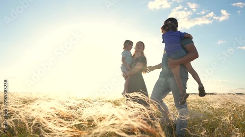 The woman and man enjoy time with their children in a field. In the field, the woman carries the girl, while the man holds the boy in the evening light.