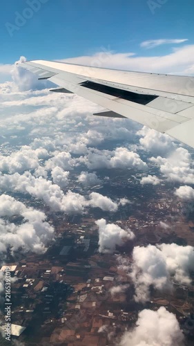 View from an airliner window showcasing a jet wing extending above clouds and rural agricultural fields. FHD vertical footage