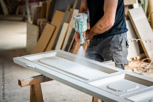 Artisan spray painting wooden door in workshop