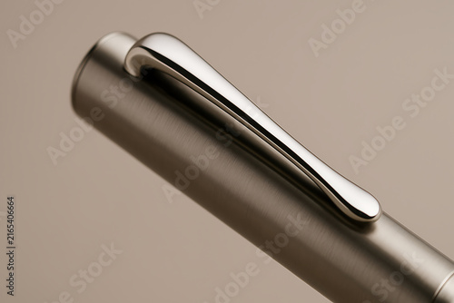 Closeup of sleek metallic pen clip on minimalist beige background with soft studio lighting