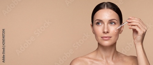 Young woman applying serum to her face with a dropper