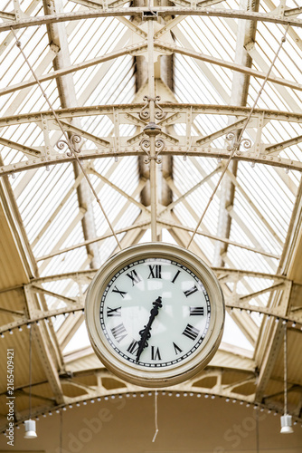 Принти на полотні Large vintage clock hanging beneath an ornate glass and iron station roof