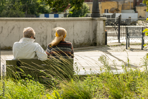 Two adult women sitting together on bench and relaxing in urban park during sunny summer day