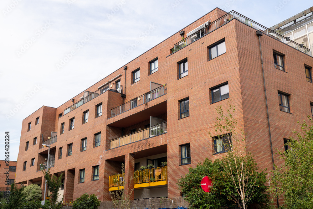 Fototapeta premium Modern Brown Brick Apartment Building Under Blue Sky With Trees and Balconies