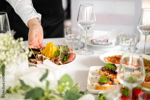 A waiter serves appetizers on a decorated wedding table with wine glasses and food.