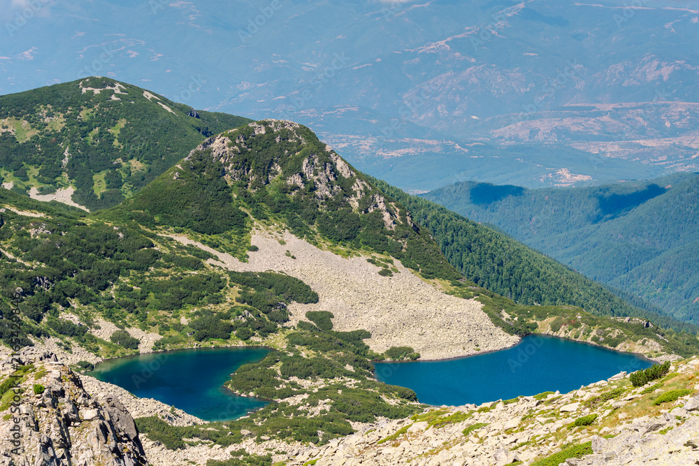 Fototapeta premium Deep blue, curved basin of the Georgiyski Lakes (Georgiyski Ezera) nestled below rugged granite slopes, scree fields, and pine-covered ridges, under a clear summer sky in Pirin National Park, Bulgaria