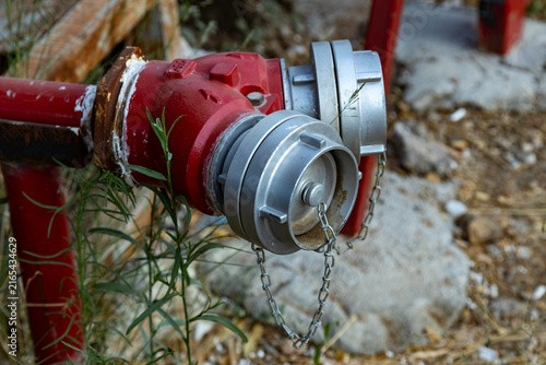 Cuadro en lienzo Close-up of a red fire hydrant valve with silver caps and protective chains connected to metal water pipes outdoors