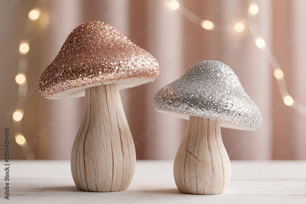 Fototapeta premium Two stylized wooden mushrooms with glittery caps sit on white surface. Rose gold, silver sparkling decor pieces stand against bokeh lights background. Rustic festive ornaments create magical