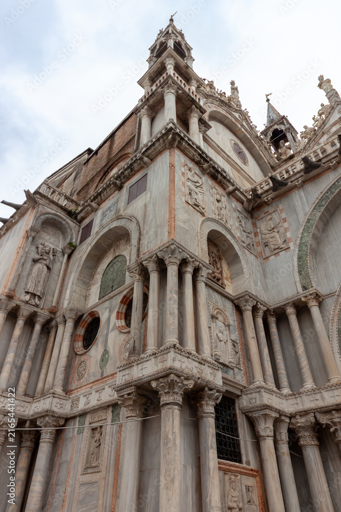 Fototapeta premium Low angle perspective of the ornate gothic marble facade and intricate stone sculptures of Saint Mark Basilica in Venice