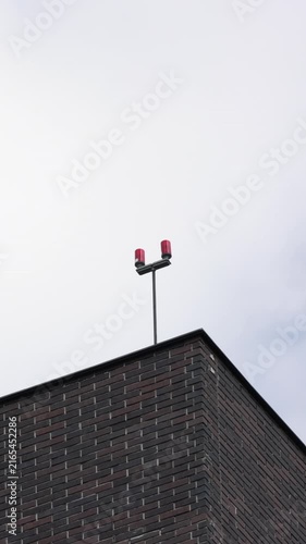 Minimalist dark brick building corner with red warning lights against overcast sky