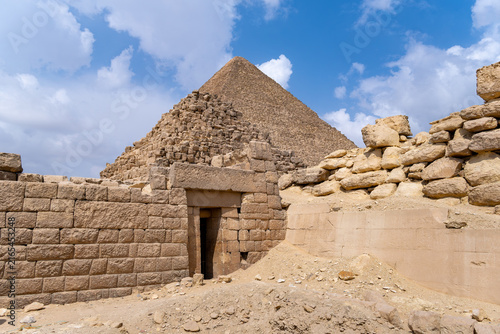 Giza pyramid standing prominently behind a weathered stone entrance and surrounding archaeological ruins in Cairo, Egypt