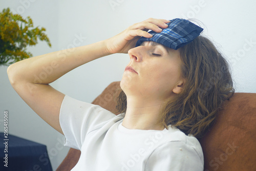 Fotografie Woman leaning back on sofa holding wet folded cloth as a cold compress on forehead