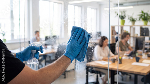 Worker Cleaning Glass Office Partition with Spray and Microfiber Cloth in Modern Workplace