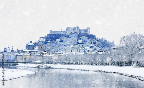 Baroque architecture of Salzburg in cold white winter landscape with falling snow and view of fortress Hohensalzburg, Cathedral Dome and church Kollegienkirche - concept of travel - Austria Europe