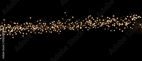 Horizontal border of glowing fairy lights against black background. Sparkling bokeh garland with warm white festive illumination. Abstract holiday banner with copy space