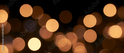 Abstract golden bokeh lights on dark background. Warm festive glowing circles banner for Christmas holiday and celebration overlay