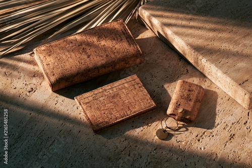 sustainable cork wallet, card holder and key case accessories arranged on natural stone surface with warm sunlight and palm leaf shadows