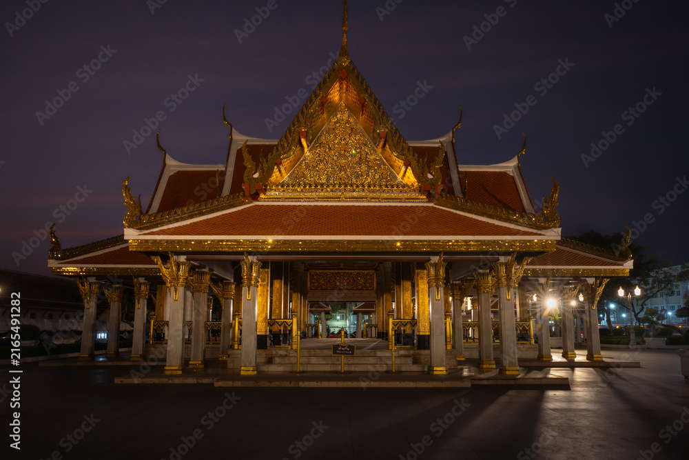 Obraz premium Traditional Thai Buddhist temple illuminated at night in Bangkok, Thailand, showcasing ornate architecture, golden details and spiritual atmosphere.