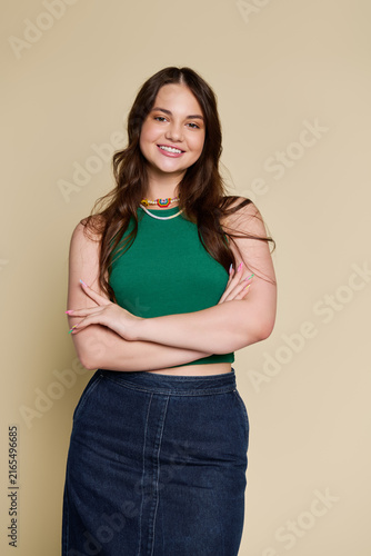 Obraz na płótnie A cheerful teenage girl poses confidently in a green tank top against a beige ba