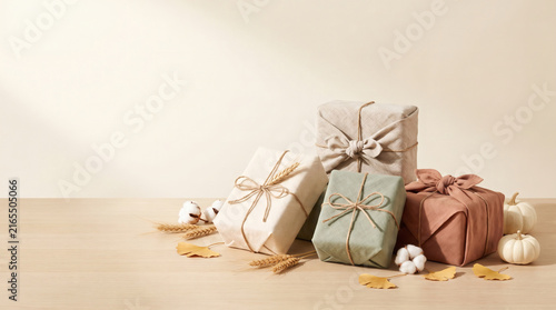 Eco-friendly fabric wrapped gift boxes with white pumpkins ginkgo leaves and copy space on wooden table