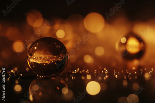 A clear crystal ball filled with liquid and bubbles sits on a reflective surface against a warm bokeh background.