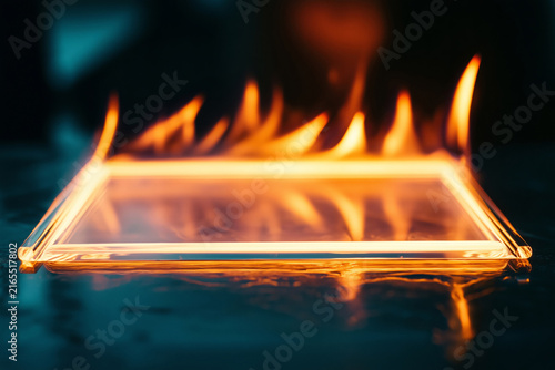 A glass tablet engulfed in vibrant flames against a dark background.