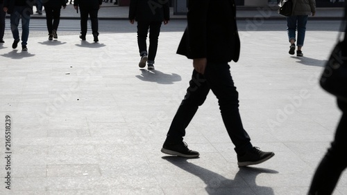 Silhouettes of people walking across a sunlit urban plaza.