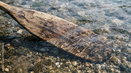 Rustic wooden boat oar resting in crystal clear shallow water over a pebbly shoreline