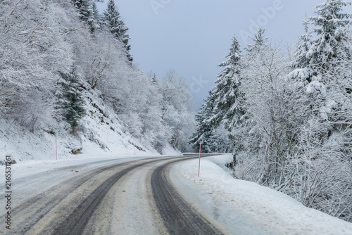 Snow-covered road winding through a peaceful winter forest in Auvergne, France, evoking a scenic road trip, mountain escape, outdoor adventure and winter travel.