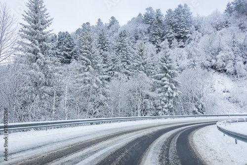 Snow-covered road winding through a peaceful winter forest in Auvergne, France, evoking a scenic road trip, mountain escape, outdoor adventure and winter travel.
