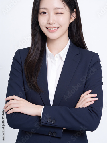 Playful young East Asian businesswoman in a navy suit winking and smiling with arms crossed in studio setting