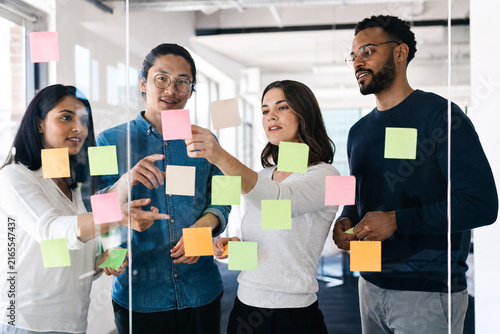 Diverse Business Team Brainstorming Creative Ideas with Colorful Sticky Notes on a Glass Wall in a Bright Contemporary Office Workspace