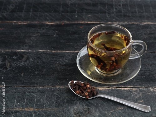 Bild auf Leinwand A glass cup of aromatic clove tea served with a spoonful of whole dried cloves on a dark wooden background