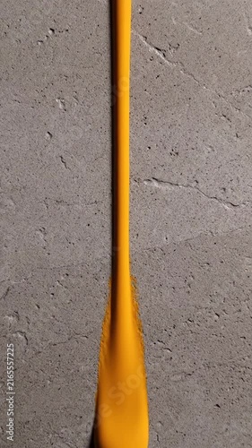 A vertical stream of vibrant yellow liquid paint flowing downward over a textured grey concrete surface background