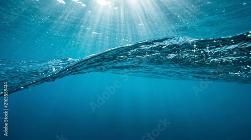 Underwater wave view with sunlight rays shining through deep blue ocean surface