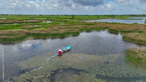 Aerial landscape of An Giang, Vietnam, showing a lone boat navigating flooded wetlands, reflective water channels, green fields, and seasonal floodplain scenery.