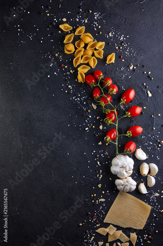 Ingredients for cooking pasta on a black background. Pasta, sherry tomatoes, garlic, cheese, pepper and salt.