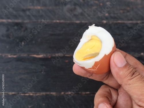 Quadro su tela Close up of a human hand holding a hard boiled chicken egg cut in half, showing the bright yellow yolk inside