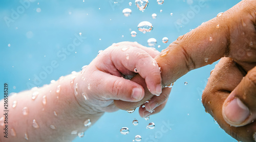 A baby's tiny hand grasps an adult's finger in clear water, bubbles rising around them. Podcast cover for themes of early connection and parental bonding.