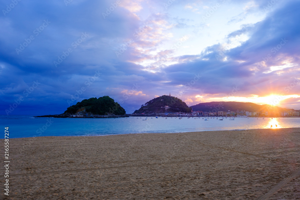Fototapeta premium Sunrise in La Concha Bay, San Sebastian Donostia, Basque Country, Spain. Scenic view of Urgull mountain and city skyline.