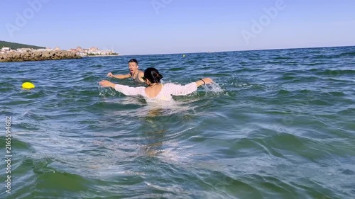 Mature mother and teenager playing ball in shallow ocean water near sandy shore during bright summer resort trip. High quality FullHD footage