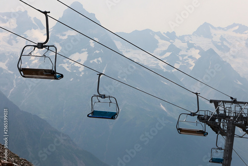 Empty chairlift seats suspended over snowy mountains