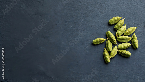 Fresh Green Cardamom Pods Scattered Over a Dark Textured Stone Surface Background